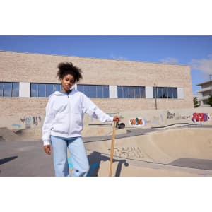 An oversized hooded jacket in white, worn by a person standing at a skatepark with graffiti.