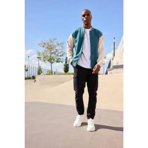 A varsity jacket in teal and cream, worn over a white shirt, paired with black cargo pants and white sneakers.