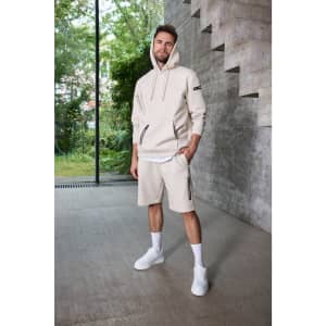 A cream-coloured men's hoodie with a zippered pocket, paired with matching shorts. Features branding on the sleeve.