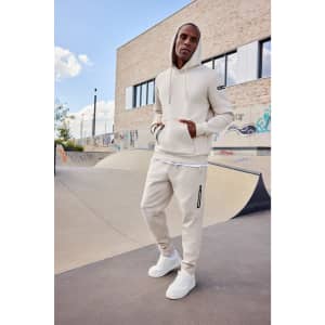 A men's interlock hoodie in beige, paired with matching pants, features a logo and a relaxed fit.