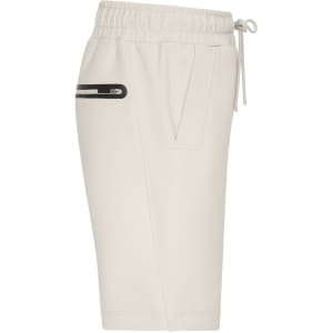 A pair of cream sports shorts featuring an elastic waistband and a side pocket with a zip.