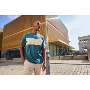 A colour-block T-shirt in teal and white, worn by a person outdoors near modern architecture.