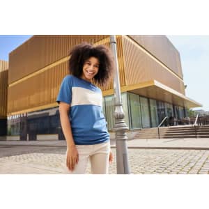 A colour-block T-shirt featuring blue and beige sections, displayed outdoors with a modern building in the background.