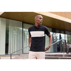 A polo shirt featuring a black base with a cream colour-block design, displayed outdoors. It has a logo.