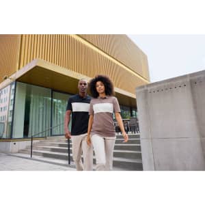 Two individuals wear colour-block polo shirts, one in black and white, and the other in brown and white, walking outdoors.