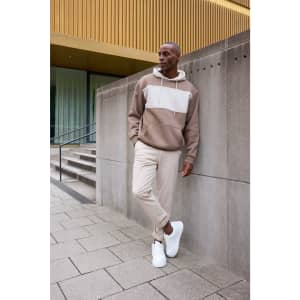 A colour-blocked sweat hoodie in earthy tones, paired with light beige pants and white sneakers, featuring a logo.