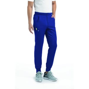 A man stands wearing blue joggers with an elastic waistband and side pockets, paired with grey shoes.