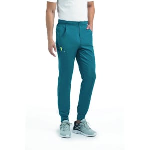 A man in a teal jogger with half elastic waistband, featuring pockets and a logo, paired with light grey shoes.