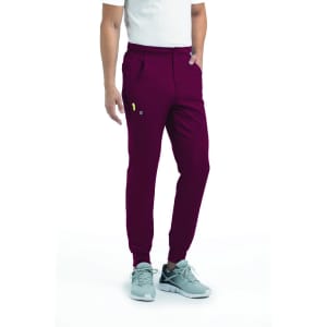 A pair of men's joggers in burgundy with a half elastic waistband and pockets, paired with grey sneakers.