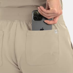 A pair of beige women's joggers featuring a pocket, holding a smartphone. The joggers have a logo on the side.
