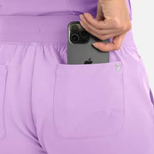 A pair of lilac joggers featuring back pockets, with a phone being placed in one pocket. Branded logo visible.