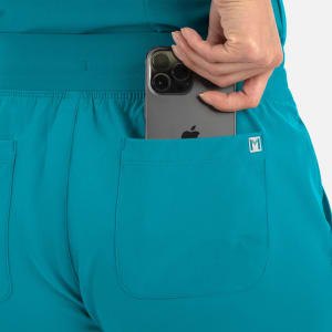 A pair of turquoise women's joggers with a pocket. A hand is placing a smartphone into the pocket.