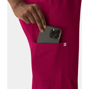 A close-up of a hand placing a smartphone into the side pocket of fuchsia skinny pull-on pants. The pants feature a logo.
