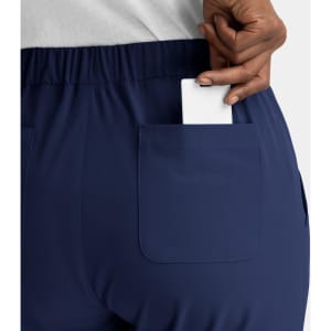 A close-up of a person's back pocket featuring a white card being inserted into navy blue pull-on pants.