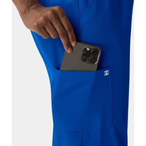 A close-up of a hand placing a phone into the pocket of bright blue women's skinny pull-on pants, featuring a logo.