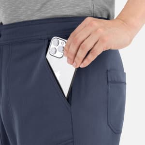 A person placing a smartphone into the side pocket of navy cargo pants featuring a half elastic waistband.
