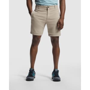 Beige dress shorts displayed on a model, featuring a logo on the waistband and styled with outdoor footwear.