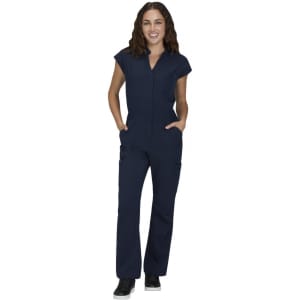 A woman wearing a navy jumpsuit with short sleeves and pockets, standing confidently. The outfit has a subtle logo.