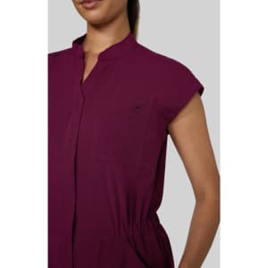 A close-up of a maroon jumpsuit featuring short sleeves and a collared neckline. It has a pocket detail and an elastic waistband.