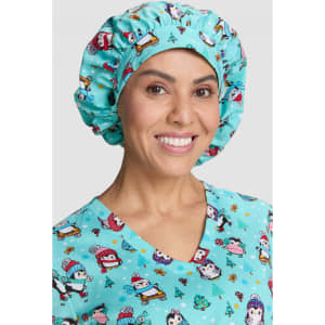 A bouffant scrub cap in light blue featuring a penguin pattern, worn by a smiling woman.