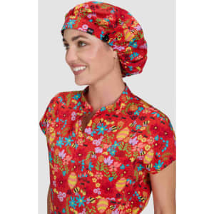 A bouffant cap featuring a vibrant floral print in red, worn by a smiling person. The cap has a logo on it.