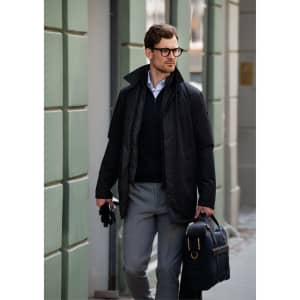 A black jacket worn over a dark sweater, paired with grey trousers and a stylish bag, featuring a logo.