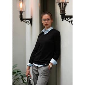 A black knitwear jumper paired with a light blue shirt and styled with grey trousers, featuring a logo.