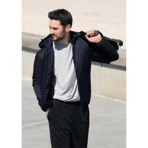 A man wearing a navy jacket with a hood, carrying a drink bottle over his shoulder. The background is a blurred outdoor setting.