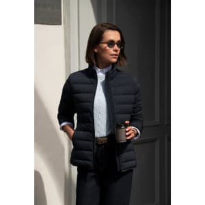 A woman wearing a navy blue down jacket, sunglasses, and holding a coffee cup, standing against a light background.