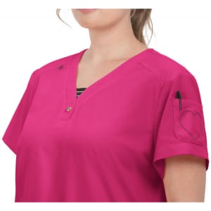 A pink top with a V-neck and short sleeves, featuring a pocket with a heart design and a pen holder.