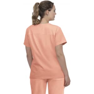 A woman wearing a peach-coloured medical scrub top, showing the back view with a simple design. The top has a logo.