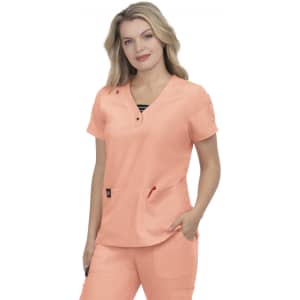 A woman wearing a light coral scrubs top, featuring short sleeves and pockets, with a slight V-neck design.