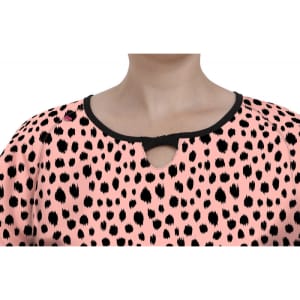 A top featuring a pink background with black spots and a decorative keyhole neckline. It has a logo near the shoulder.