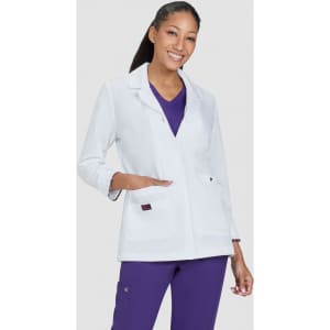 A white lab coat with a button front and pockets, worn over a purple top, modelled by a smiling woman.