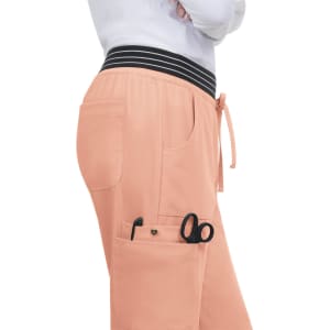 A pair of soft peach-coloured jogger pants featuring pockets and a striped waistband, with scissors visible in one pocket.