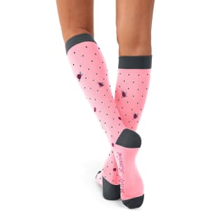 A pair of pink compression socks with polka dots and a logo, featuring a grey cuff and sole.