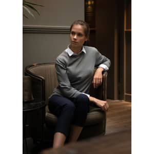 A grey knitted jumper worn over a white collared shirt, featured on a seated model in a stylish indoor setting.