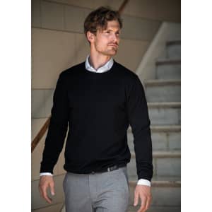 A man wearing a black knitted jumper with a white shirt, walking down a staircase. The jumper has a logo.