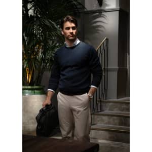 A knitted jumper in navy worn by a man, paired with light trousers, standing near a staircase with greenery.