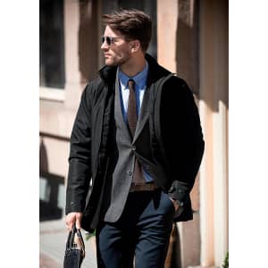 A stylish black men's jacket worn over a grey blazer with a light blue shirt, paired with sunglasses and trousers.
