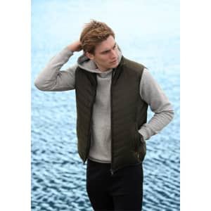 A green puffer vest worn over a grey hoodie, modelled by a young man against a water background.