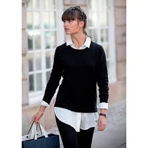 A woman wearing a black knitted jumper over a white shirt, carrying a shopping bag in an urban setting.