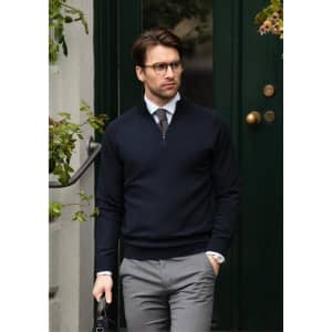 A stylish navy 1/4-zip men’s knitwear, paired with a shirt and grey trousers, featuring a logo on the chest.