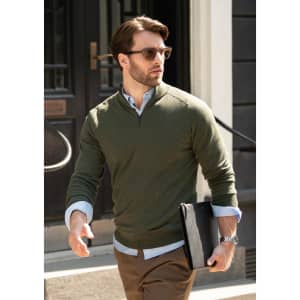 A man wearing an olive green 1/4-zip knitwear top with sunglasses, holding a black folder, walking outside.