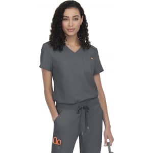 A woman wearing grey scrubs with a v-neck design and an orange logo, posing confidently with her hands on her hips.