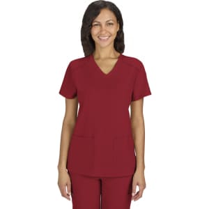 A red scrubs top with a V-neck design and two front pockets, worn by a smiling woman. The garment features a logo.