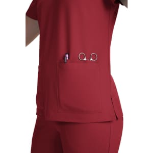 A red scrub top featuring a large pocket containing a pen and scissors, with a simple design and no visible logos.