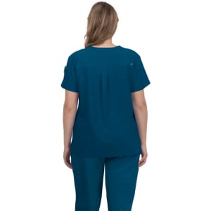 A women's scrub top in teal, featuring a relaxed fit and back pleat design. It has a brand logo on one sleeve.