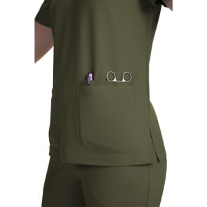 A green scrub top with a side pocket featuring a pen and scissors. The top has a simple design and a fitted look.