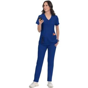 A woman wearing a blue scrub top and matching pants, holding a smartphone and standing in a relaxed pose.